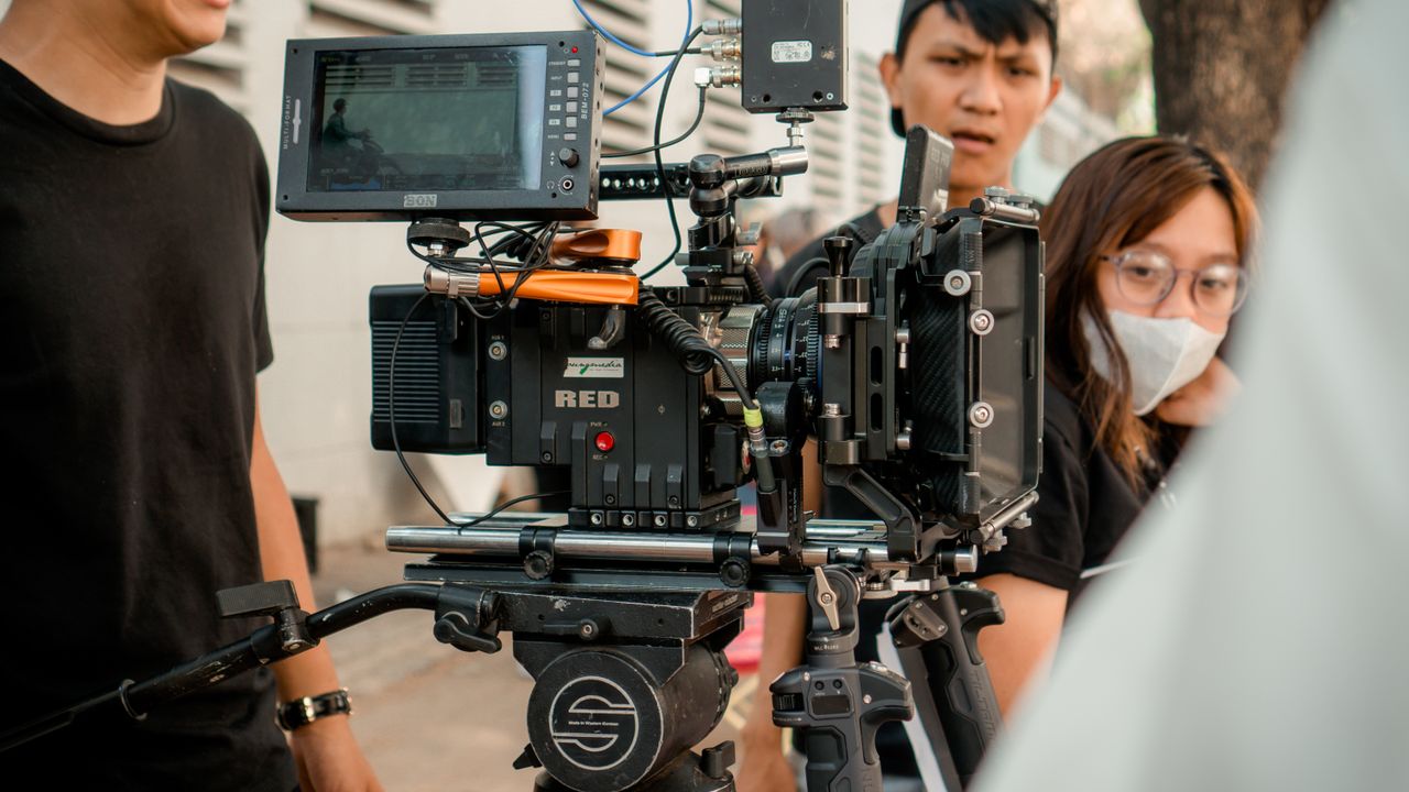 Close-up of a professional film camera setup with crew members on an outdoor set.