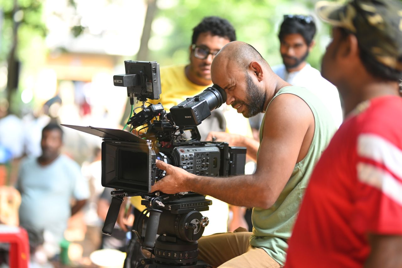 Filmmaker using a professional video camera on an outdoor set, surrounded by crew members.